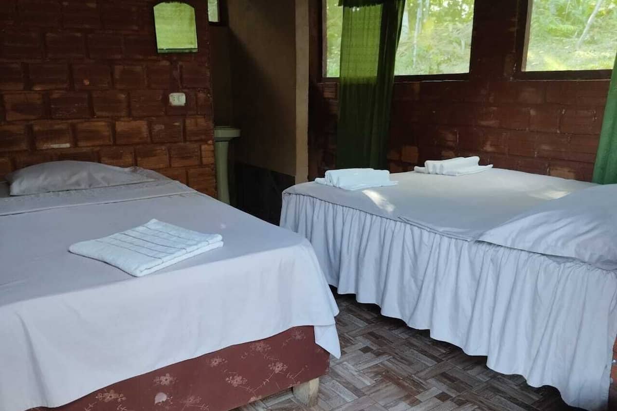 Two single beds with white linens, a brick wall, and a window with green curtains.