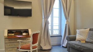 A living room with a sofa, a chair, a desk with a computer, and a TV on the wall. - Locanda San Tomaso (Pietra Ligure)