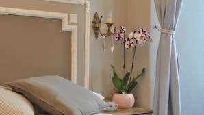 A neatly made bed with a pillow, a bedside table with a vase of orchids, and a wall-mounted candelabra. - Locanda San Tomaso (Pietra Ligure)