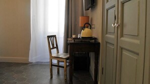 A room with a wooden chair, a small table with a kettle, a television mounted on the wall, and a door with a handle. - Locanda San Tomaso (Pietra Ligure)