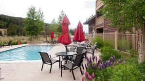 A pool area with lounge chairs and umbrellas, surrounded by greenery and a wooden fence. - 1BR/2 FULL Baths +Murphy bed & Sleeper Sofa, Sleeps 6, to Gondola in 337 steps (Keystone)