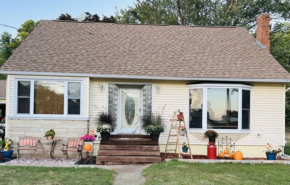 A single-story house with a front porch, a wooden bench, and potted plants.