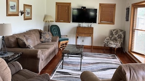 A living room with a brown leather sofa, a green armchair, a small table, and a flat-screen TV mounted on the wall.