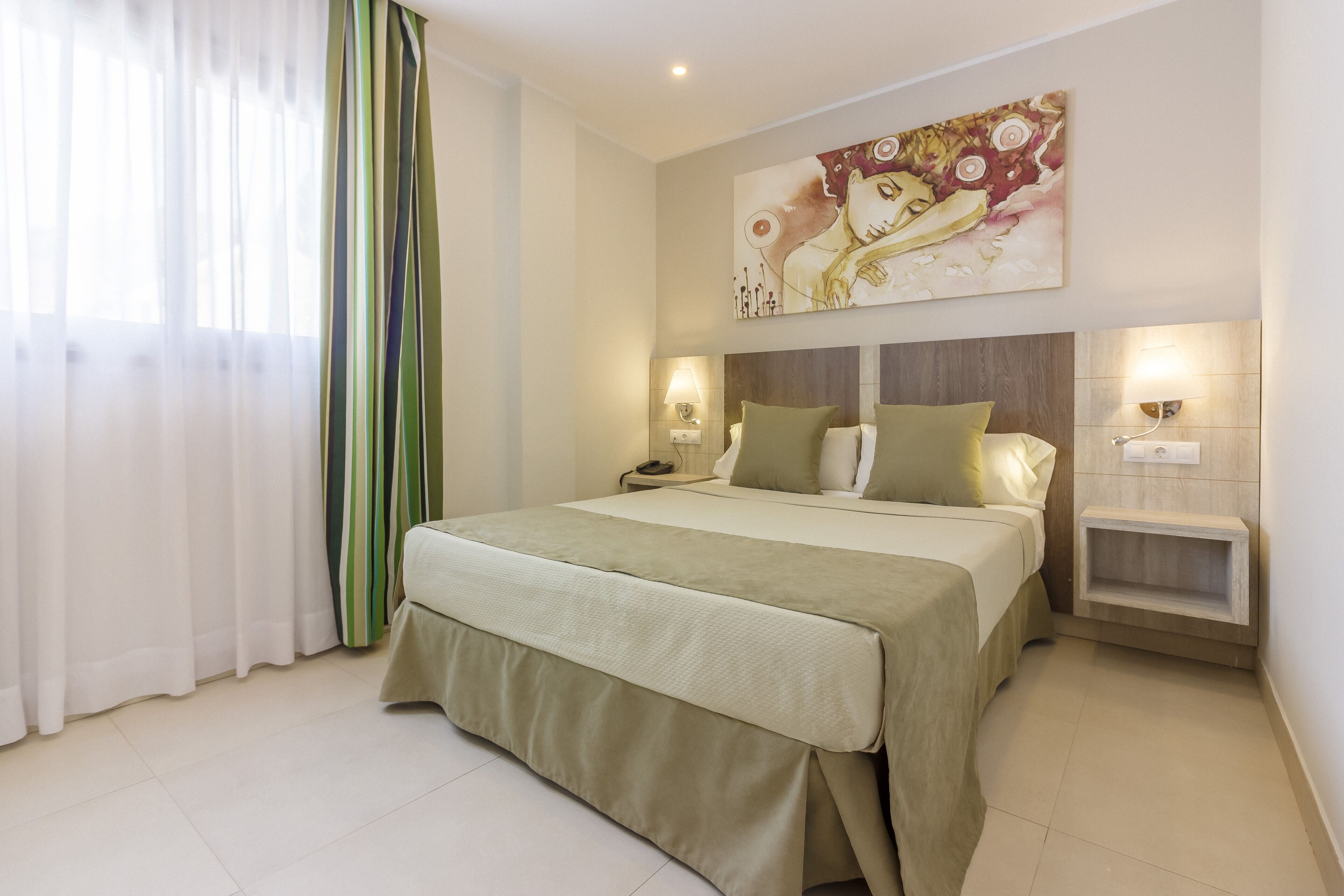 Un dormitorio con cama, mesitas de noche, lámpara de pared y un cuadro.