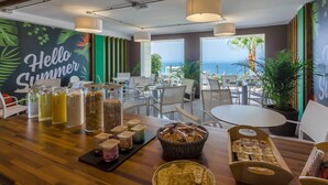 A restaurant with a view of the ocean, featuring a 'Hello Summer' mural, various food and drink options, and a casual seating arrangement.