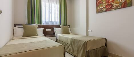 A hotel room with two beds, a window with curtains, a painting on the wall, and a bedside table.