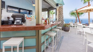 A bar area with a counter, bar stools, and outdoor seating with umbrellas.