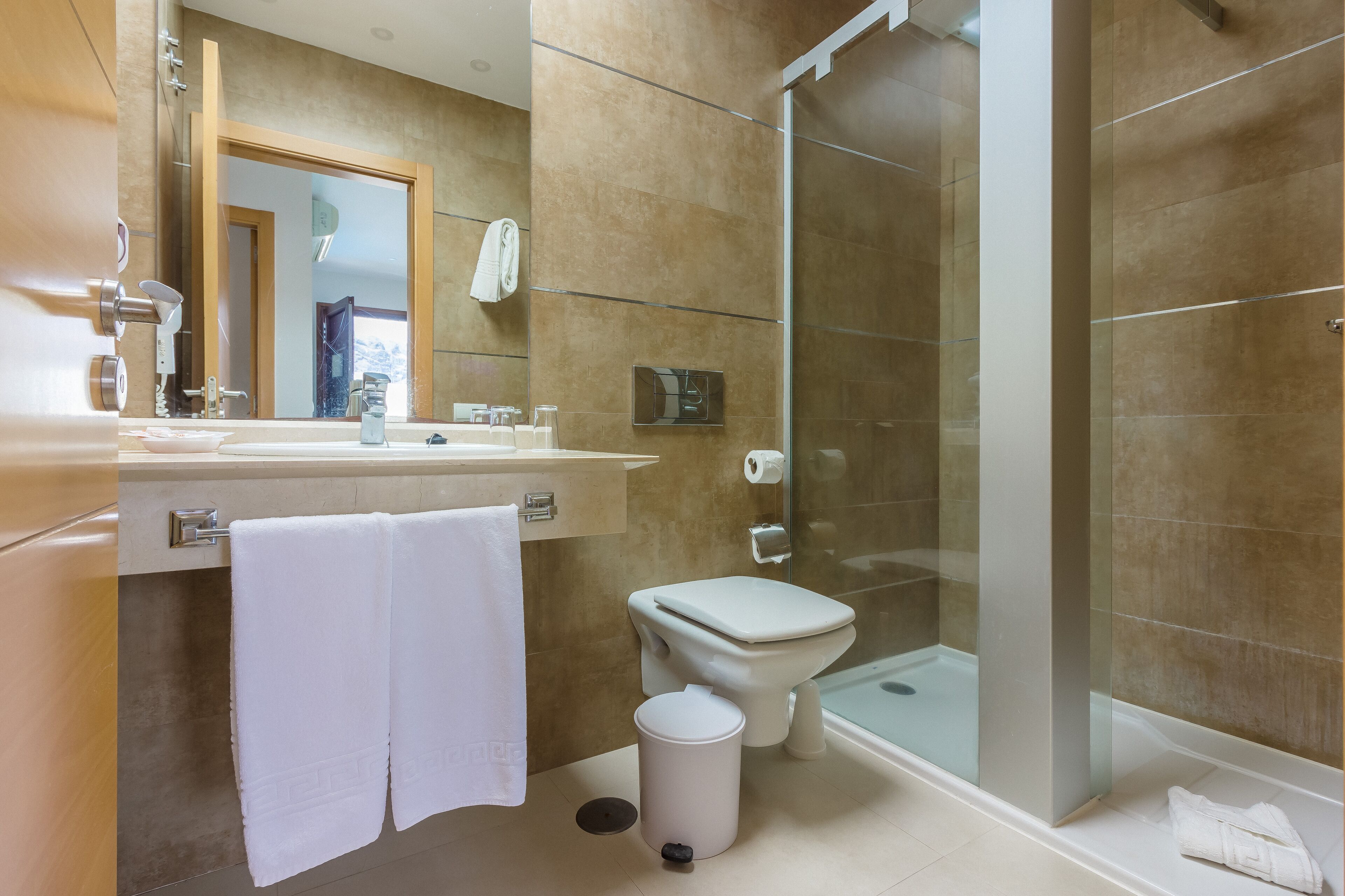 Ein modernes Badezimmer mit einer Duschkabine aus Glas, einer Toilette und einem Waschbecken. Ein Handtuch hängt an der Wand.