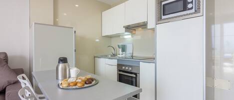 A compact kitchen with a dining area, a microwave, a kettle, and a plate of pastries.