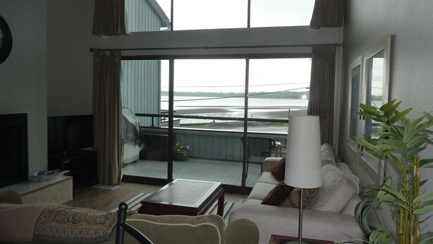 Ein Wohnzimmer mit großem Fenster mit Blick auf einen Strand, einer Couch, einem Couchtisch und einem Fernseher.
