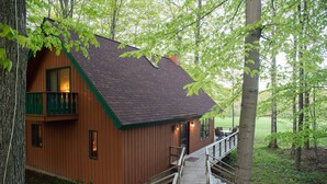 Una cabaña de madera con balcón y terraza, en un entorno forestal natural.