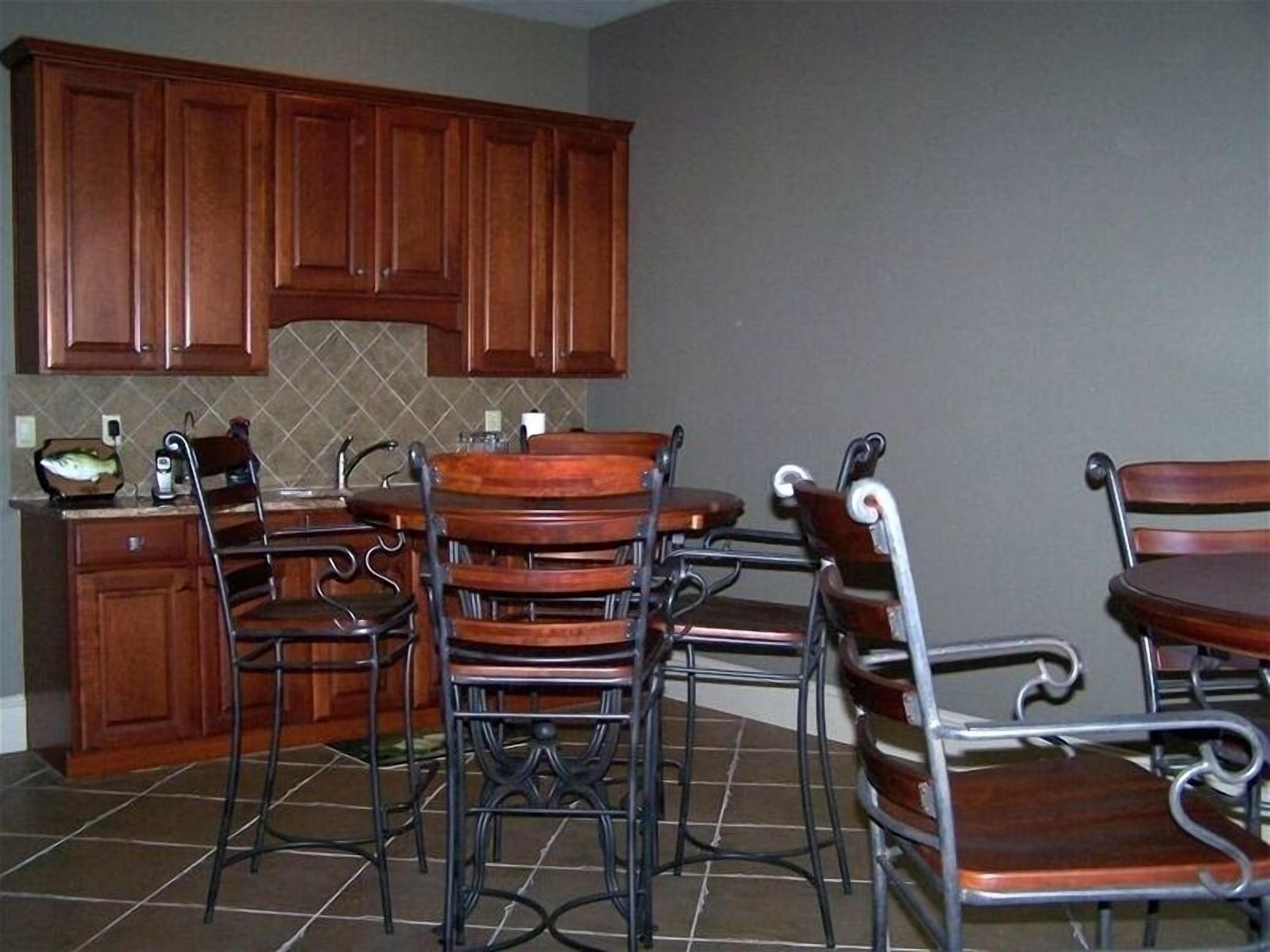 A kitchen with wooden cabinets, a tiled backsplash, and a dining area with metal chairs and a wooden table.