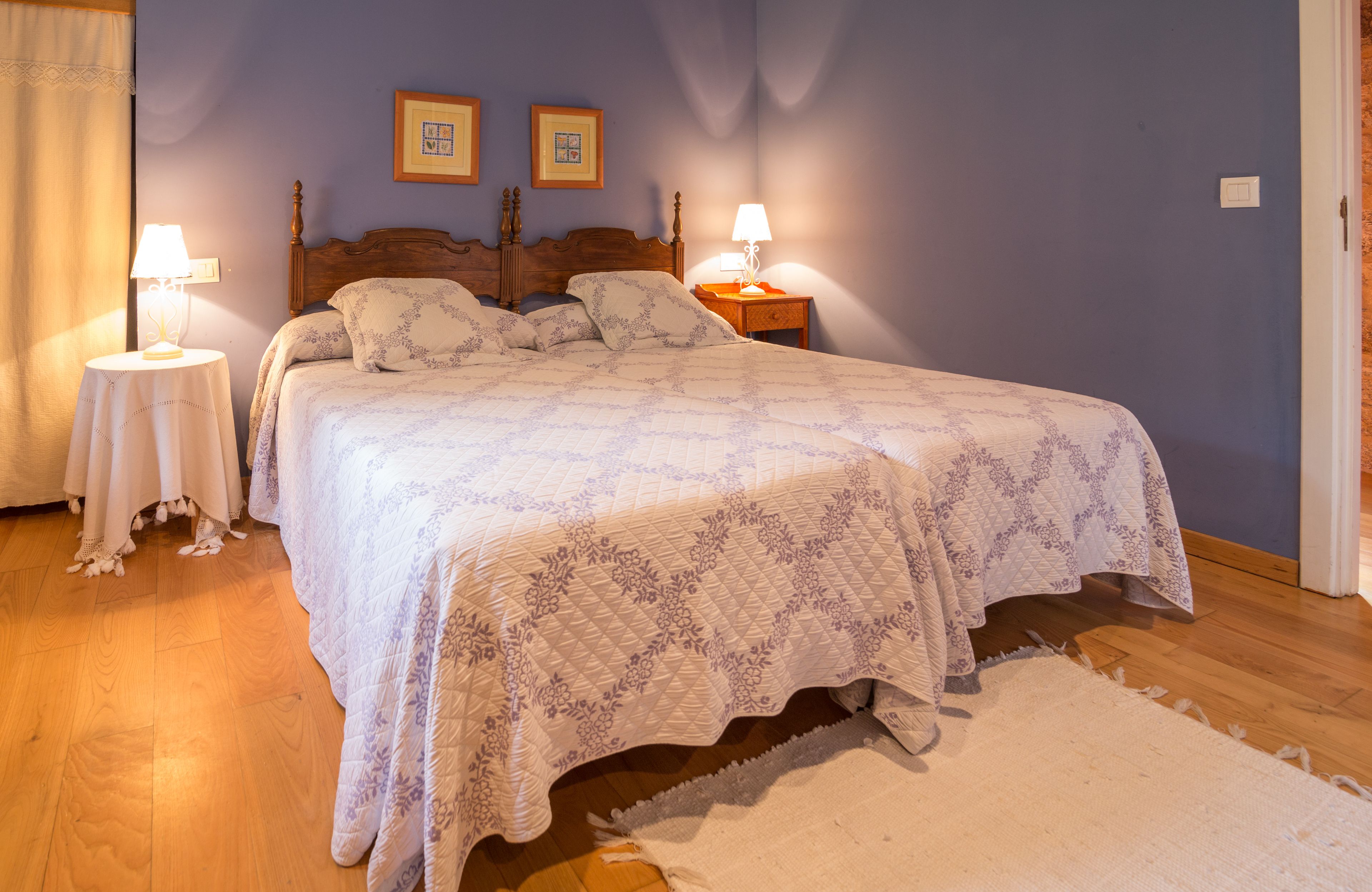 Een slaapkamer met een groot bed, twee nachtkastjes met lampen, een houten hoofdbord en twee ingelijste foto's aan de muur.