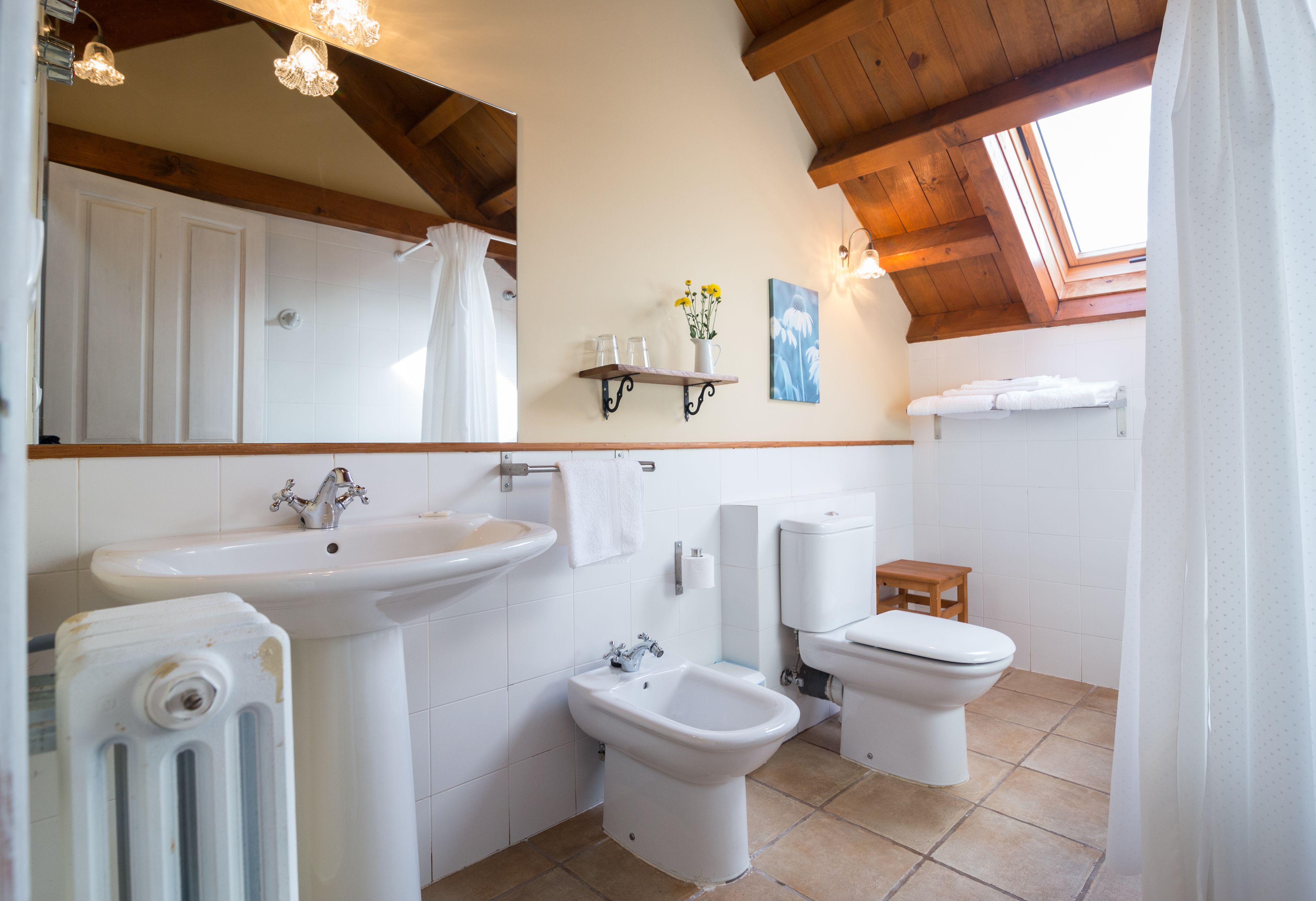 Ein Badezimmer mit Waschbecken, Bidet, Toilette und einem Holzregal mit Toilettenartikeln.