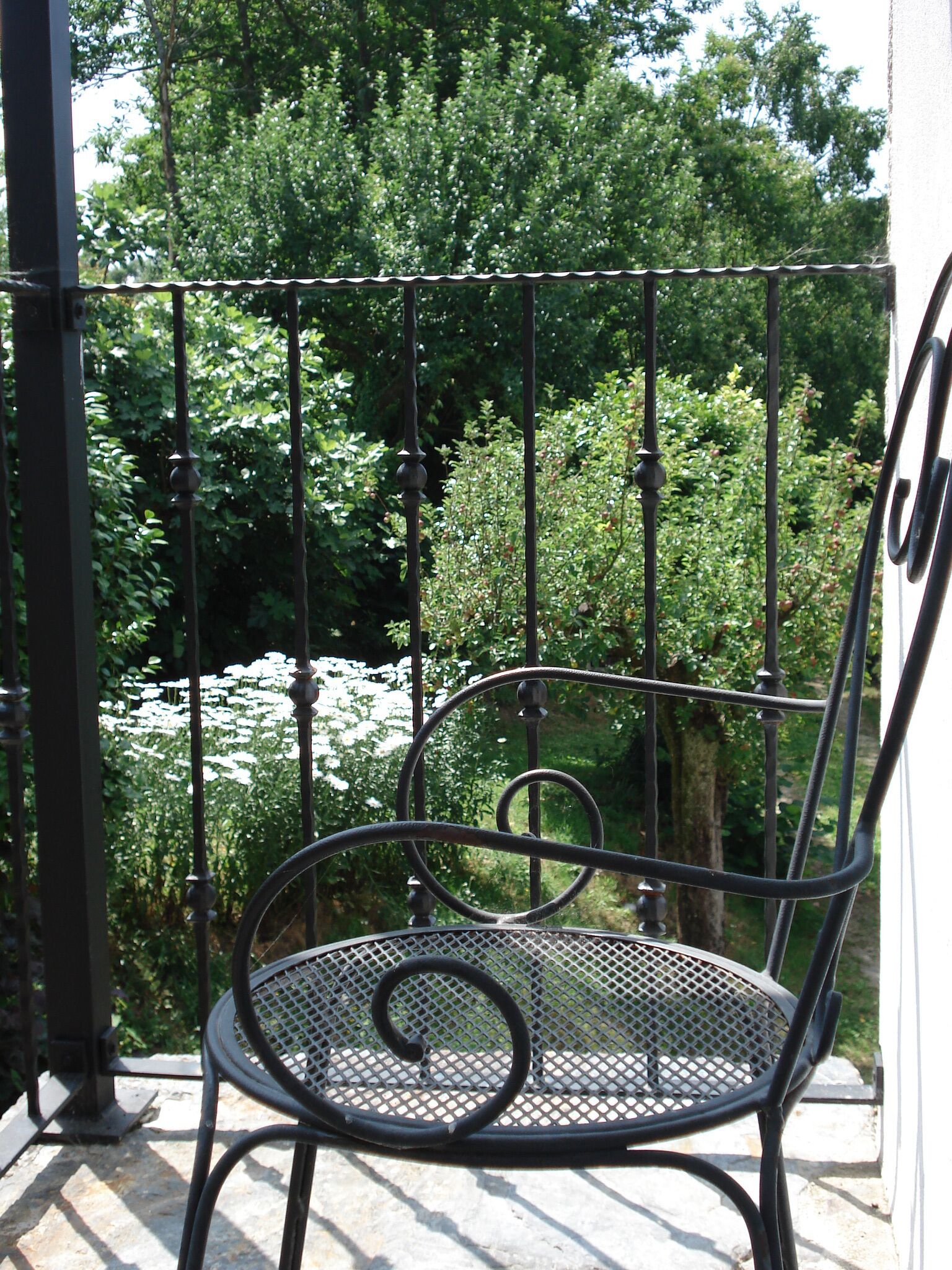 A metal chair with a spiral design on a balcony with a view of greenery.