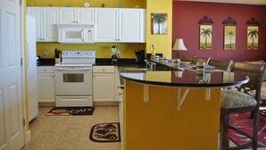 A kitchen with white cabinets, a microwave, stove, and a coffee maker. There is a dining area with a table and chairs.
