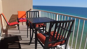 A balcony with a table and chairs, a view of the ocean, and a pier in the distance.