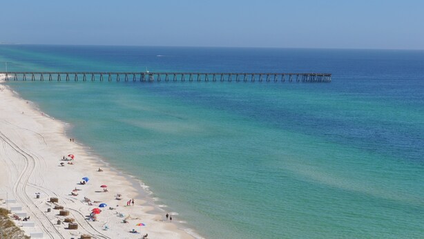 A beach with a pier extending into the ocean, clear skies, and a few people on the sand.