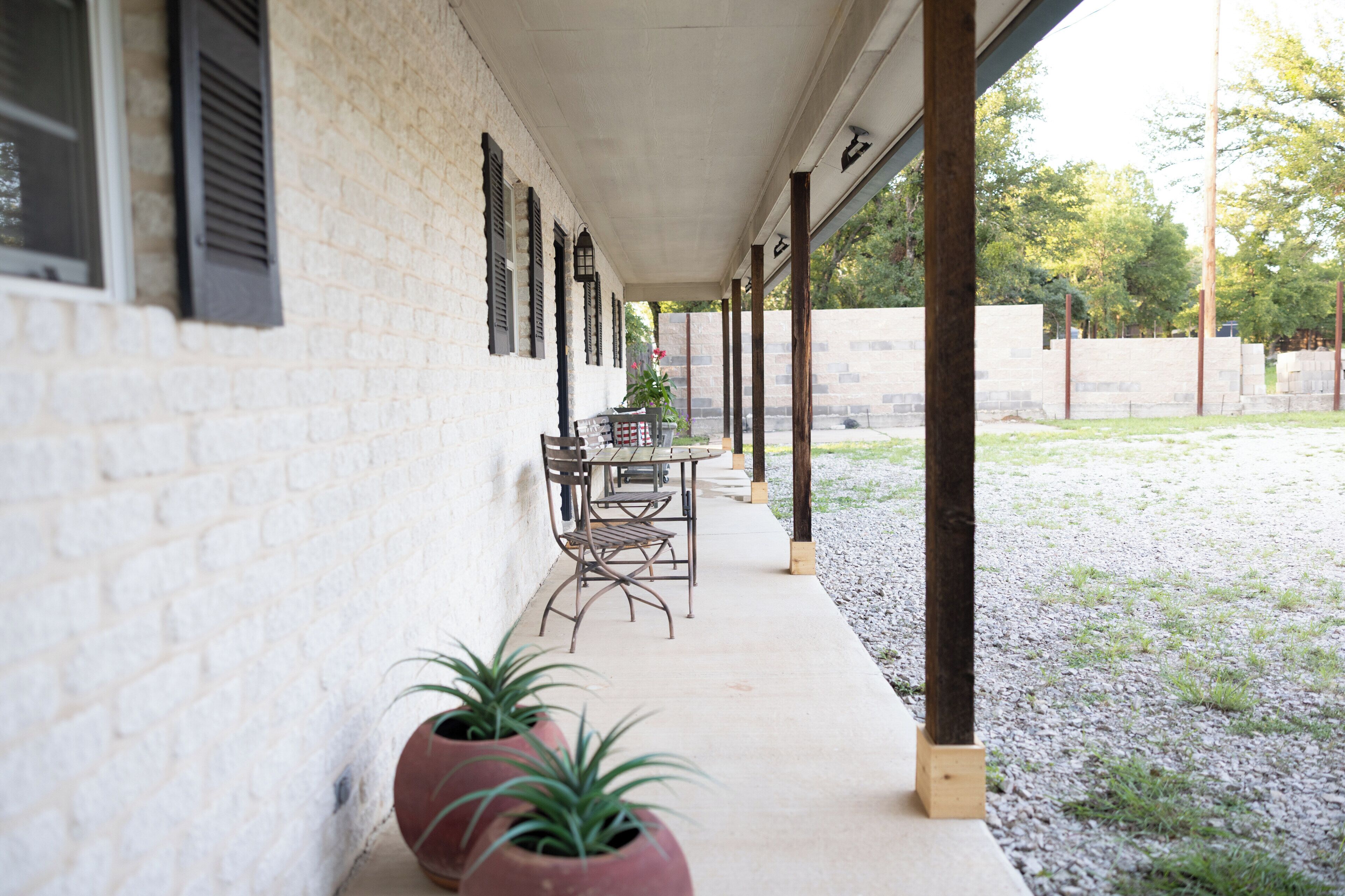 A covered outdoor seating area with a brick wall, potted plants, and a table and chairs.