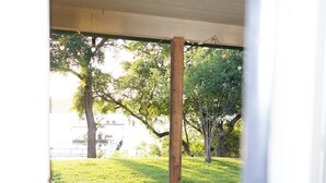 A view through a doorway with a patterned floor, a wooden column, and a green lawn with trees.