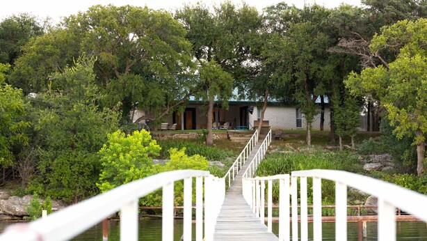 A wooden bridge leading to a stone building with a porch and outdoor seating.