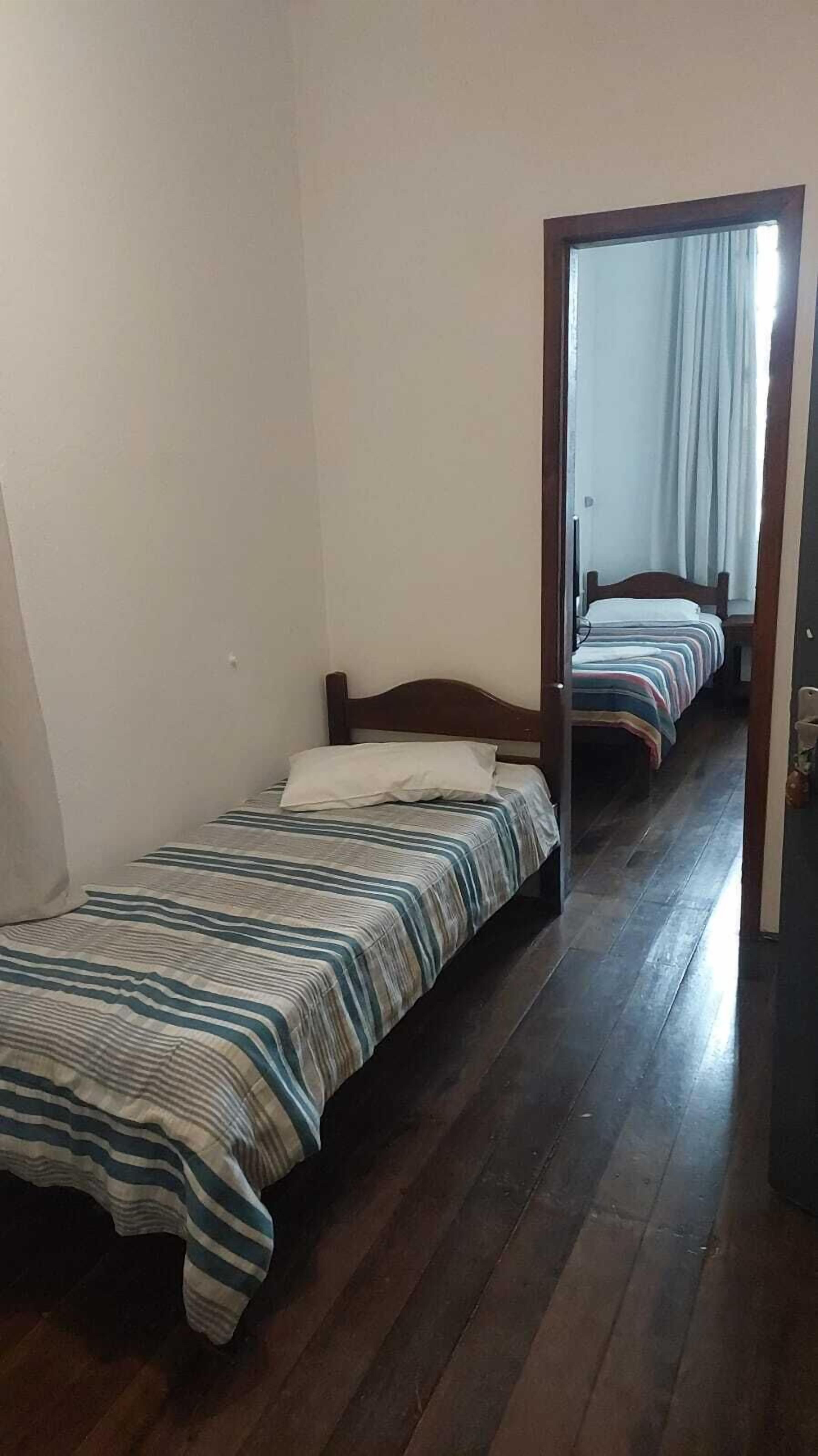 Ein Zimmer mit zwei Einzelbetten, Holzboden und einem Spiegel, der ein Fenster mit Vorhängen widerspiegelt.
