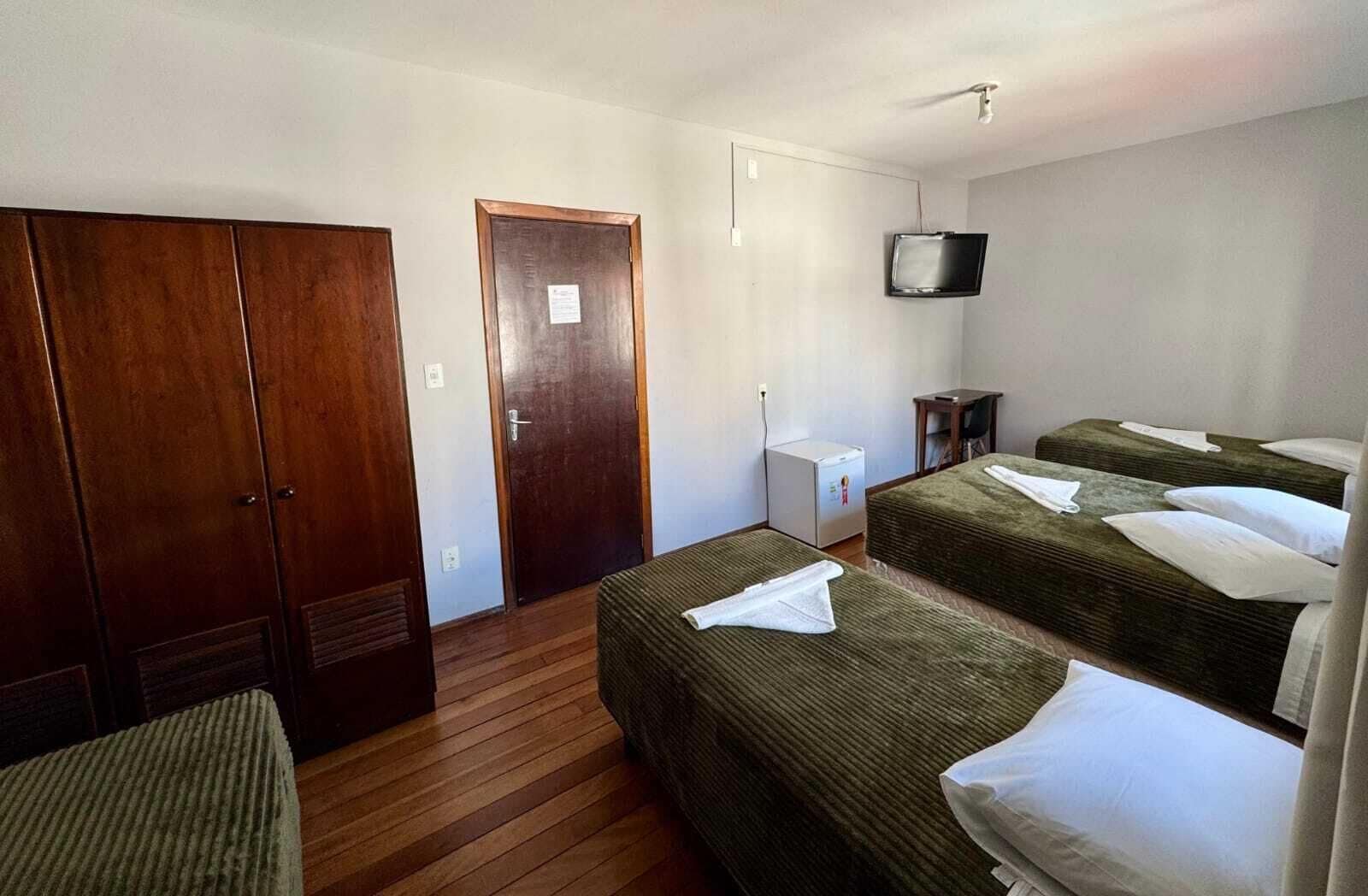 Habitación de hotel con dos camas, un armario, un televisor y una mesita.