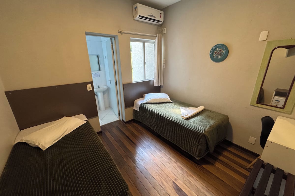A room with two beds, a window, a mirror, and an air conditioning unit.