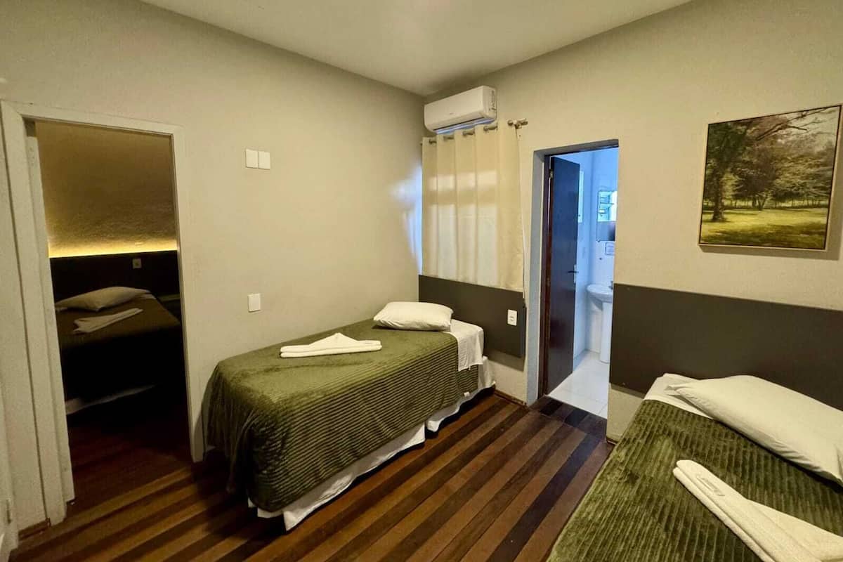 A small, compact room with two single beds, a wooden floor, a small bathroom with a sink, and a painting on the wall.