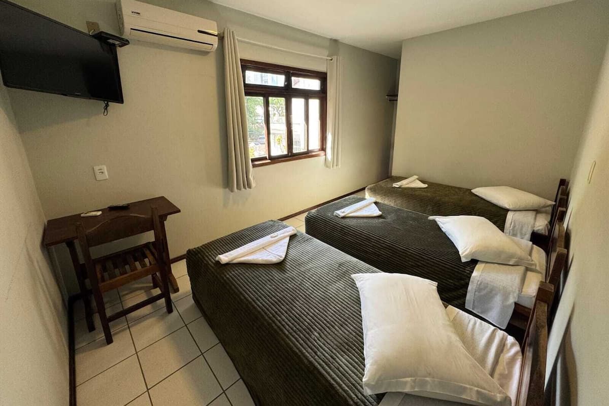 A hotel room with two single beds, a desk, a chair, an air conditioning unit, and a window with curtains.