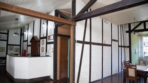 Un área de recepción con mostrador blanco, vigas de madera y un comedor con mesa y sillas.