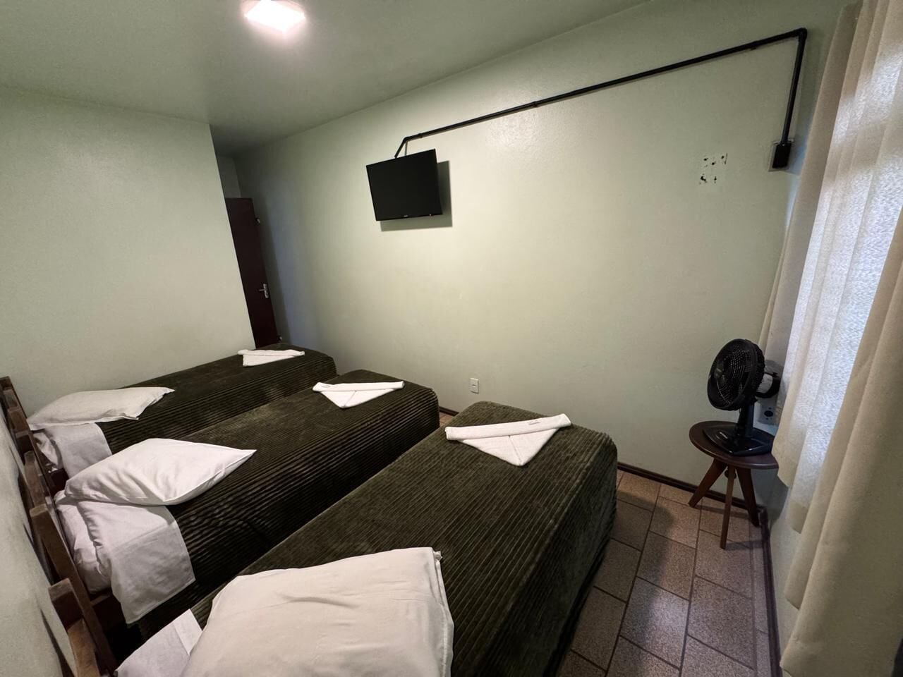 Una habitación con dos camas, un ventilador pequeño y un televisor en la pared.