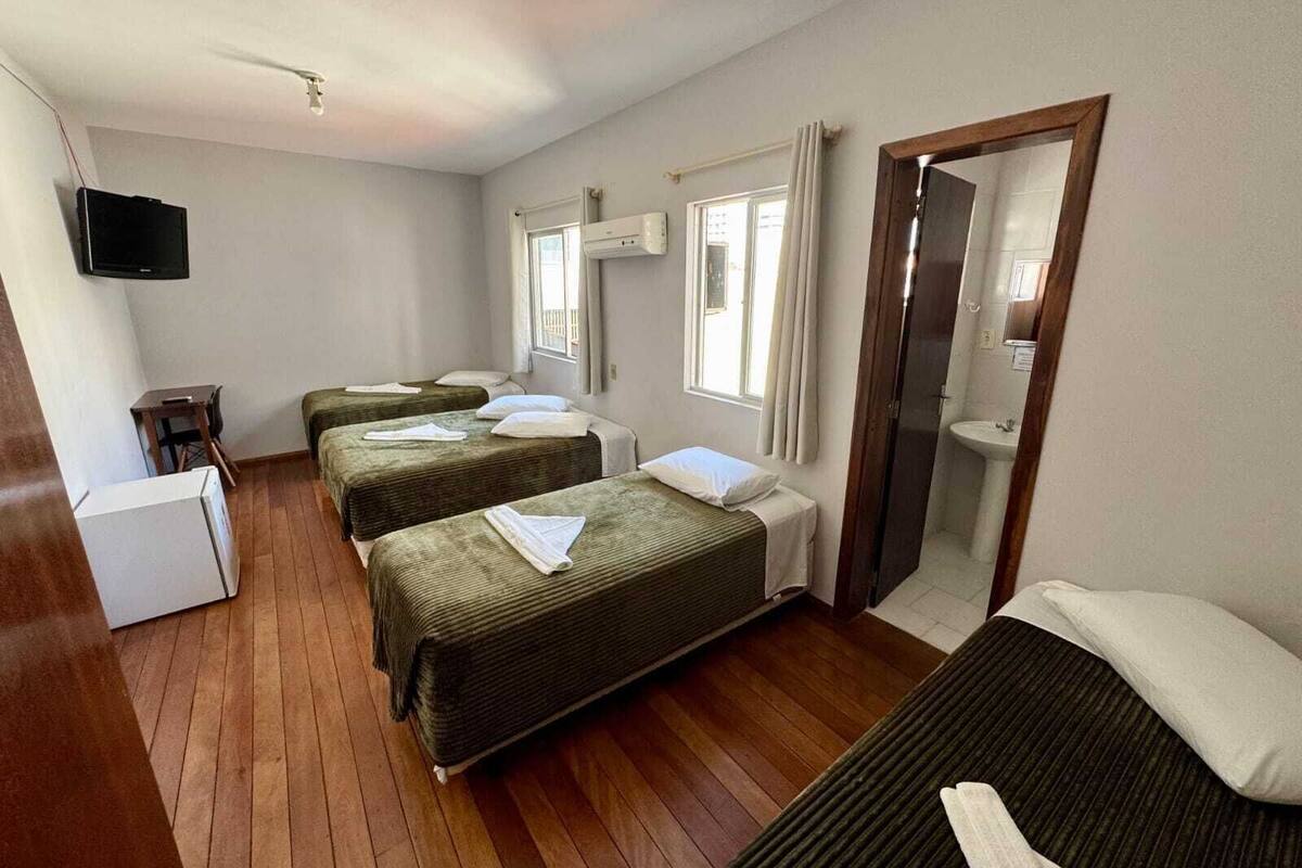 A hotel room with three beds, a small desk, a television, and a bathroom with a mirror and sink.