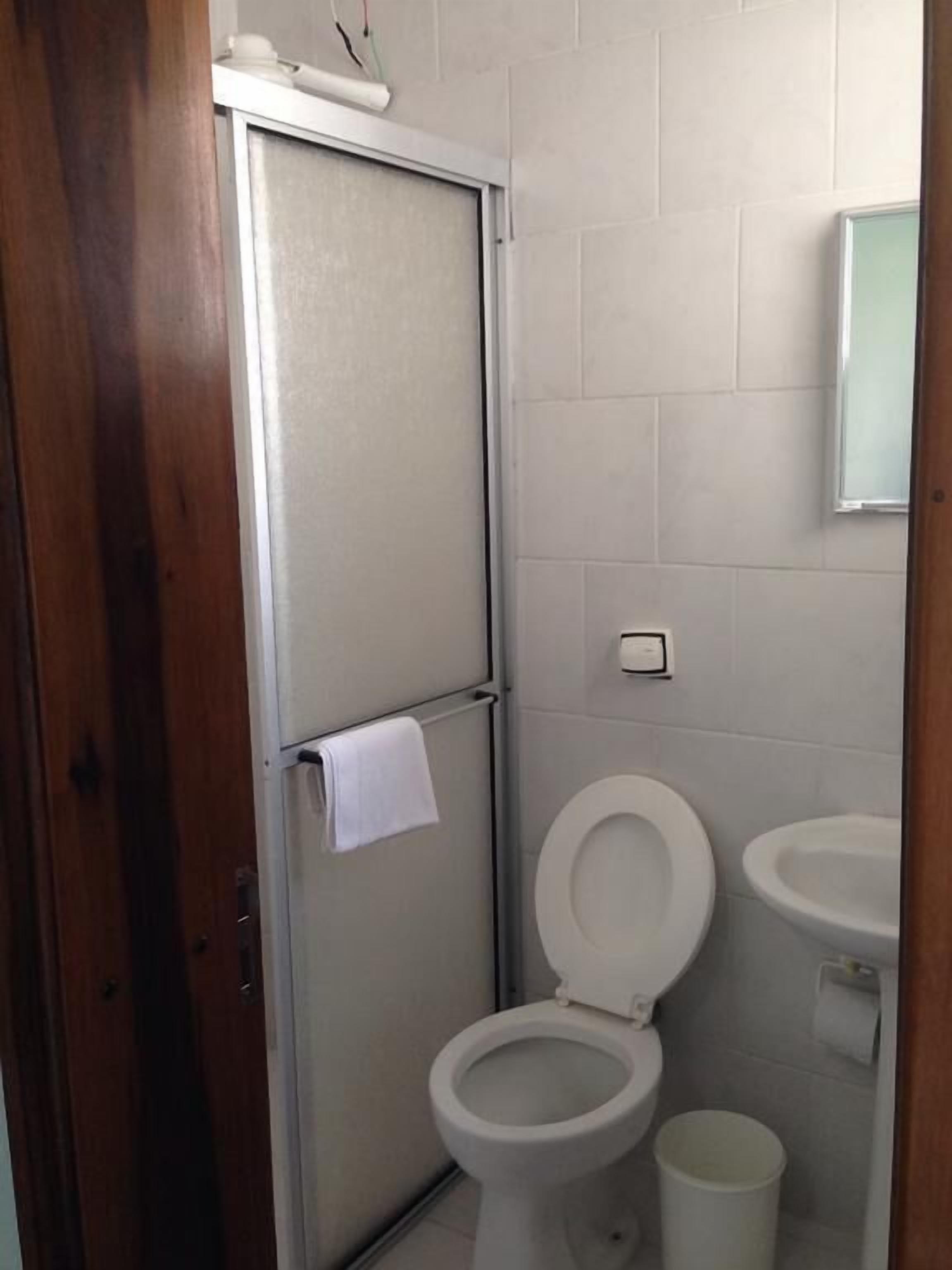 Uma casa de banho pequena e limpa, com sanita, lavatório e uma toalha pendurada na porta.