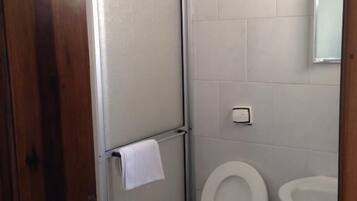 Uma casa de banho pequena e limpa, com sanita, lavatório e uma toalha pendurada na porta.