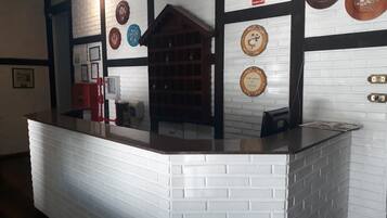 Un área de recepción con un mostrador de ladrillo blanco, una vitrina de madera y platos decorativos en la pared.