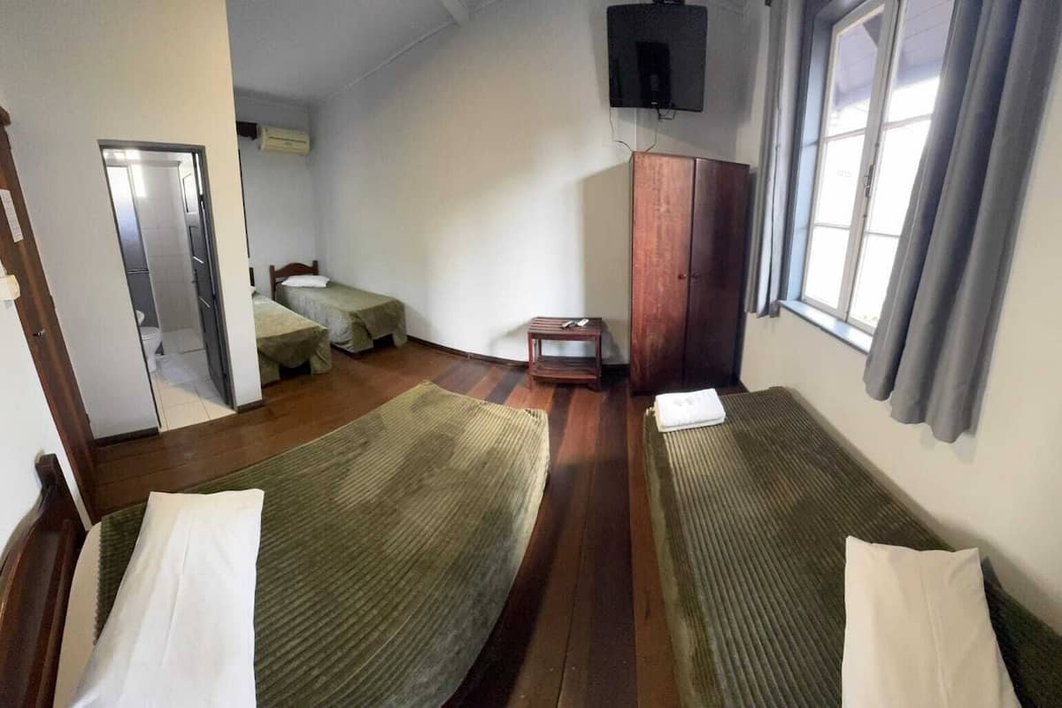A room with two single beds, a wooden wardrobe, a television mounted on the wall, and a window with curtains.