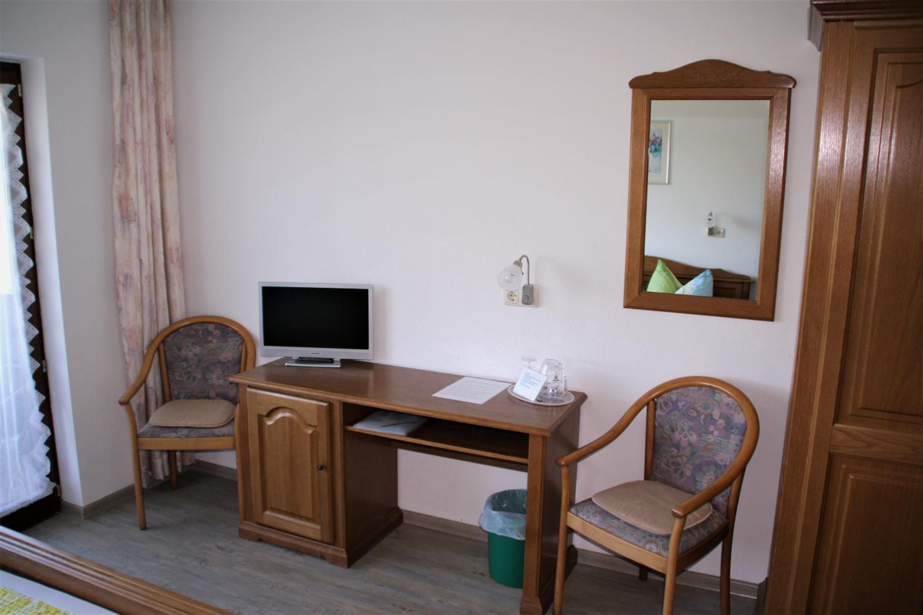 Une pièce comprenant un bureau en bois, deux chaises, un téléviseur, un miroir et une poubelle.