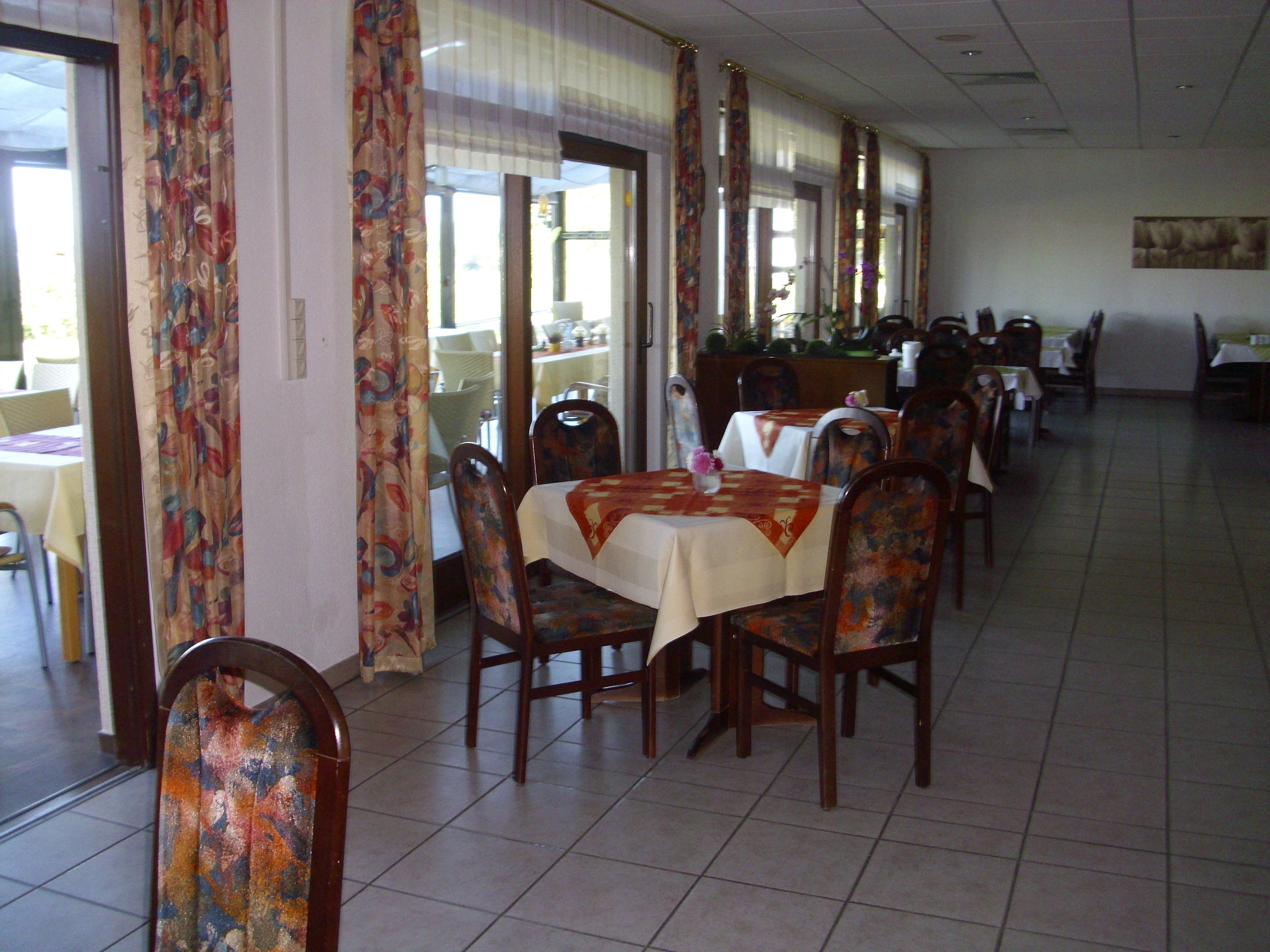 A dining area with tables and chairs, large windows, and a tiled floor.