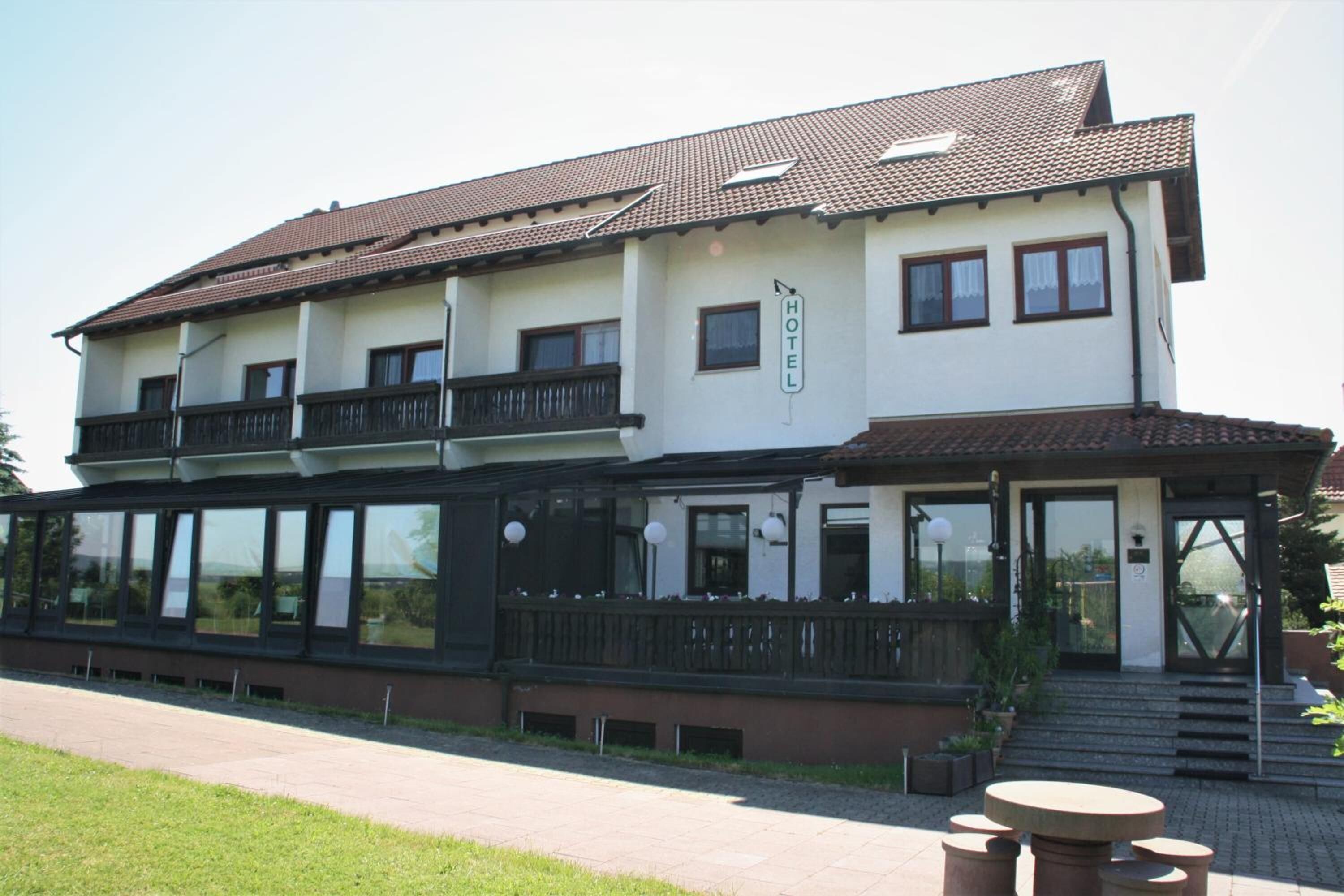Un hôtel à deux étages doté d’un balcon à l’étage supérieur, de grandes fenêtres et d’un espace d’entrée abrité.