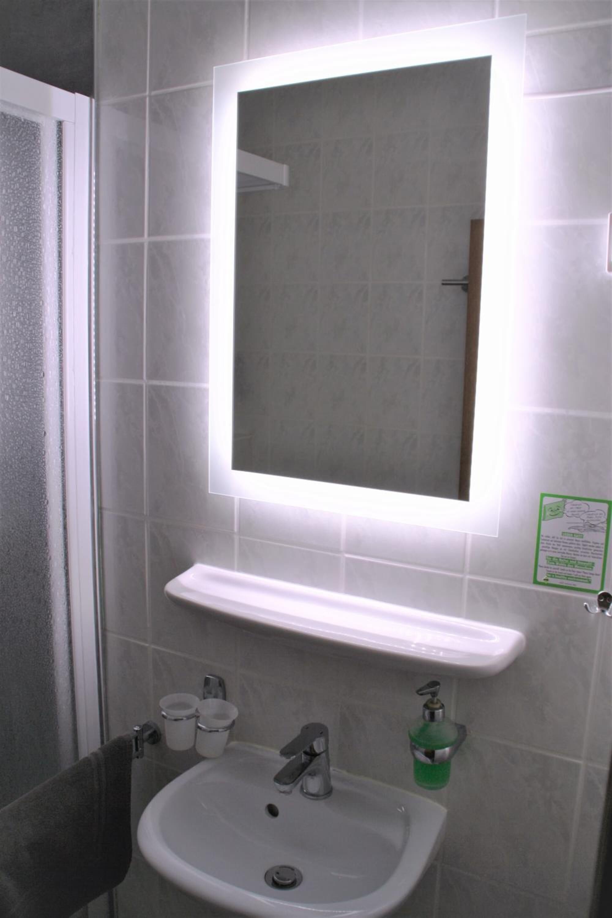 A bathroom with a white sink, mirror, and a soap dispenser.