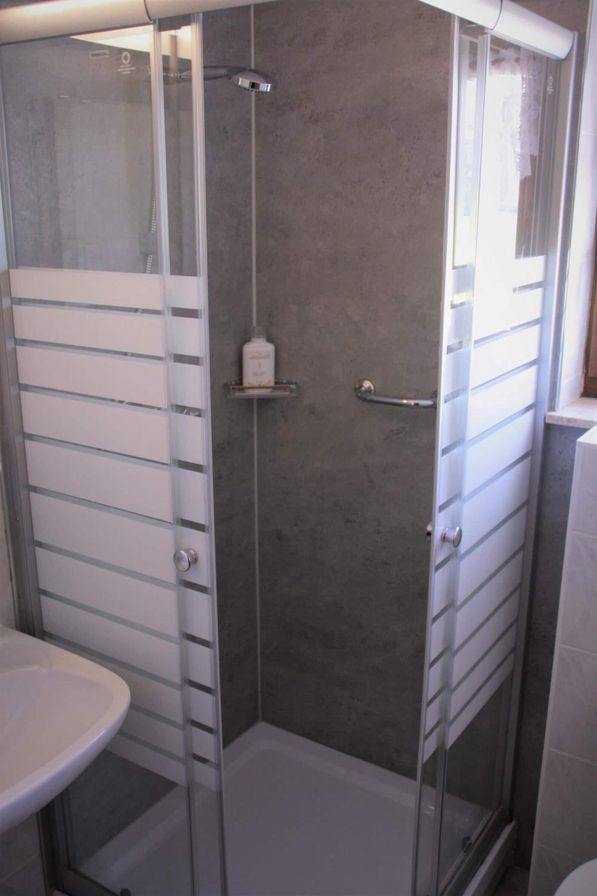 A glass-enclosed shower with a white sink and a small shelf.