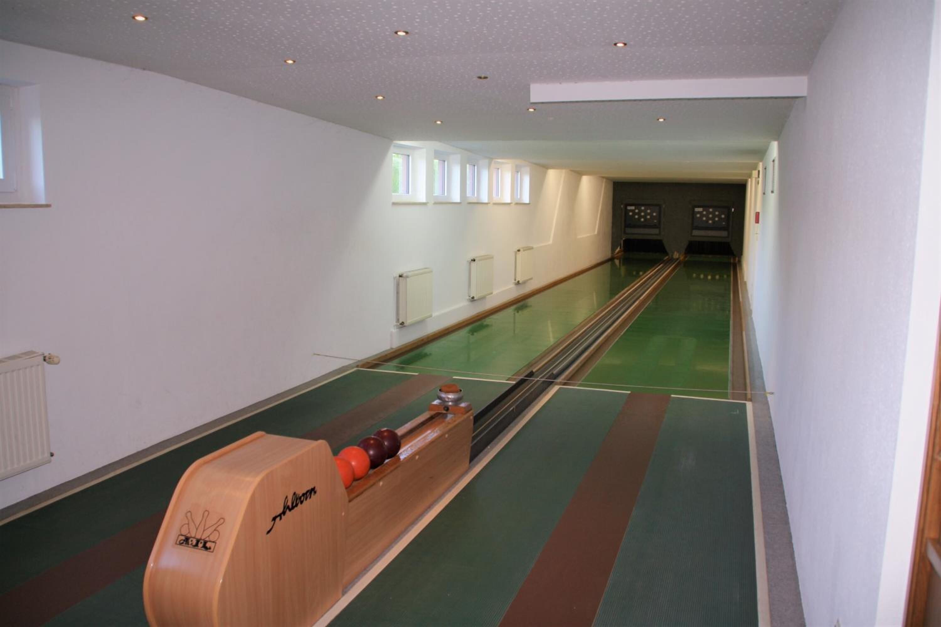 Una bolera con alfombra verde, pistas de boliche de madera y un elevador de bolas de madera.