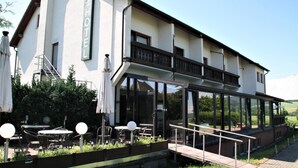 A hotel with outdoor seating, a balcony, and a glass-enclosed dining area. - Hotel Waldschlösschen (Werra-Suhl-Tal)