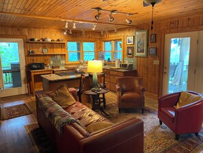 L’intérieur chaleureux d’un chalet avec un plafond en bois, un coin repas, une cuisine et un salon comprenant un canapé et des fauteuils.