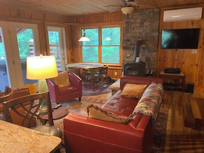 Un intérieur de chalet chaleureux avec une cheminée, un téléviseur, un coin repas et un canapé en cuir.
