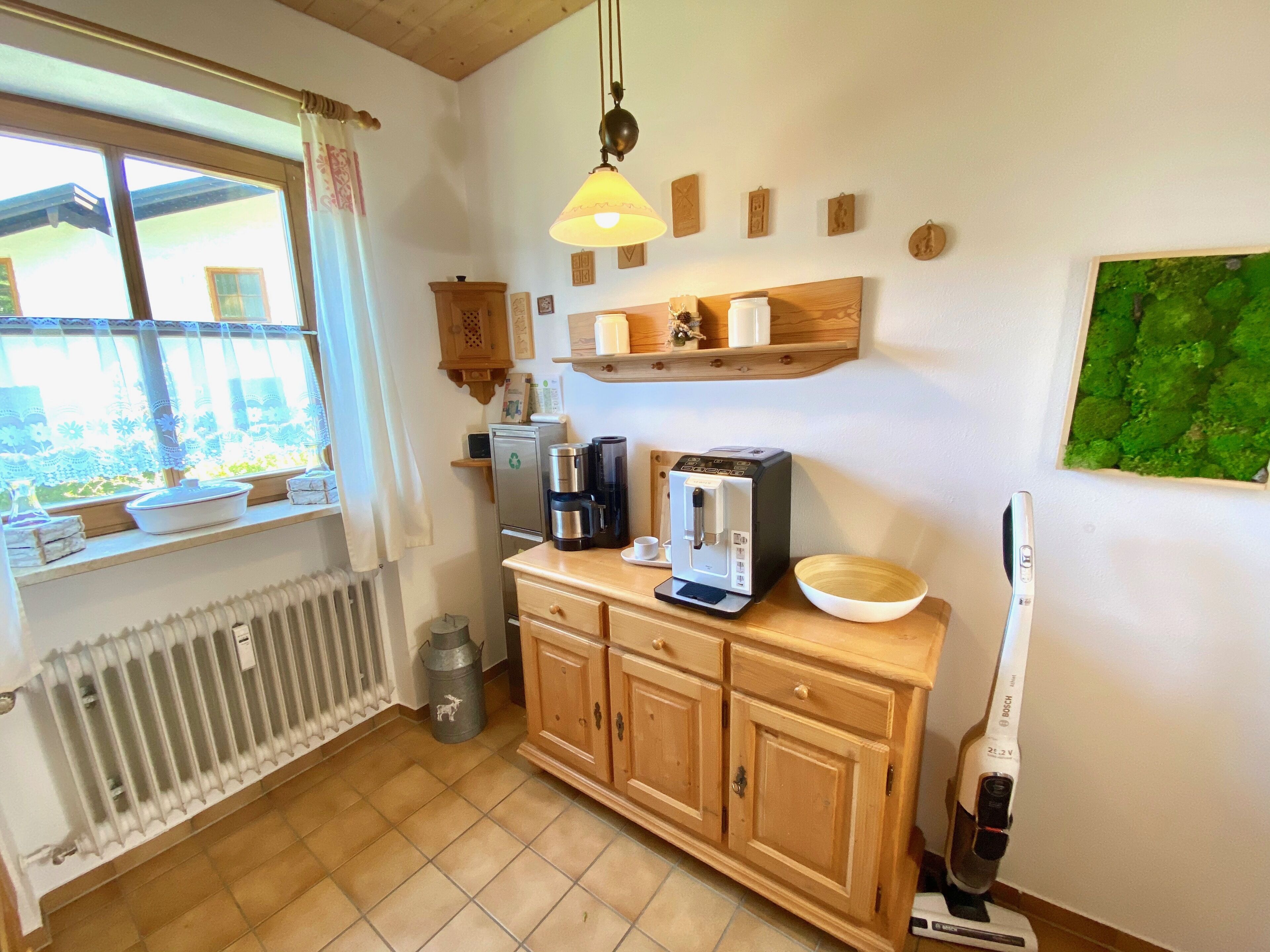 Une cuisine équipée d’une machine à café, d’un aspirateur Bosch et d’une fenêtre donnant sur un paysage verdoyant.