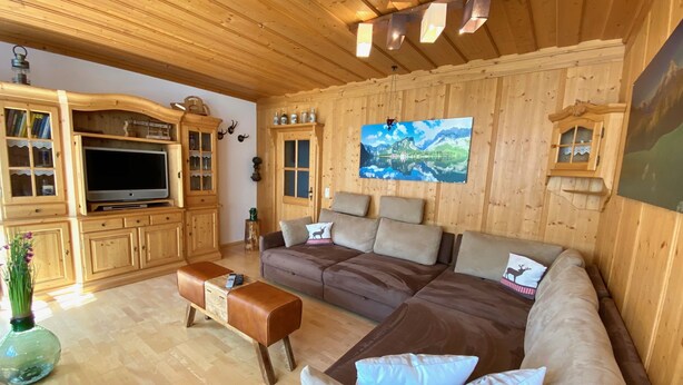 A wooden-paneled room with a large flat-screen TV, a brown sofa, and a wooden cabinet.
