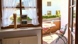 A room with a window overlooking a balcony, a radiator, and a table with a chair.