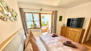 A bedroom with a bed, a wooden cabinet, a television, and a window with curtains.